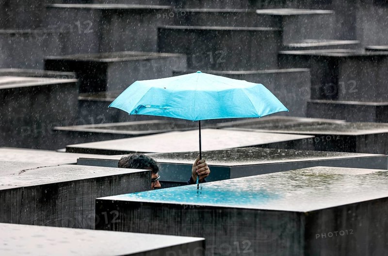 A visitor to the Memorial to the Murdered Jews of Europe protects himself from heavy rain with an umbrella, Berlin, 23 June 2023