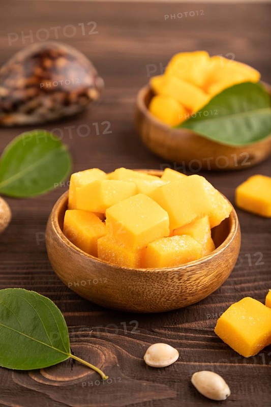 Dried and candied mango cubes in wooden bowls on brown wooden textured background. Side view, close up, selective focus, vegan, vegetarian food concept