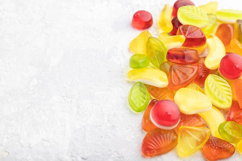 Various fruit jelly candies on gray concrete background. side view, copy space