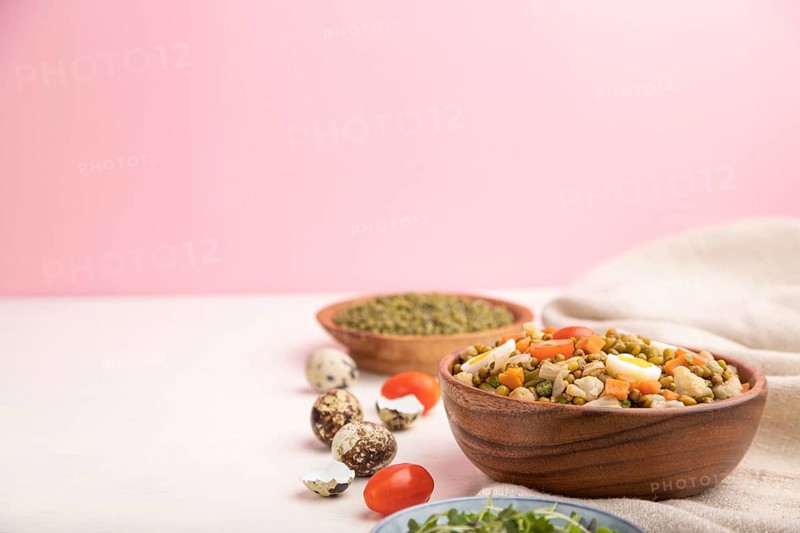 Mung bean porridge with quail eggs, tomatoes and microgreen sprouts on a white and pink background and linen textile. Side view, copy space, selective focus