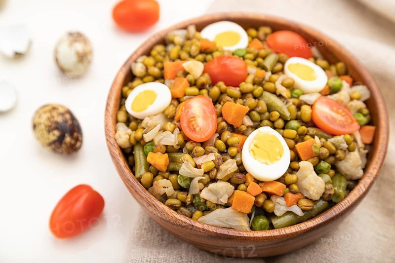 Mung bean porridge with quail eggs, tomatoes and microgreen sprouts on a white wooden background and linen textile. Side view, close up, selective focus