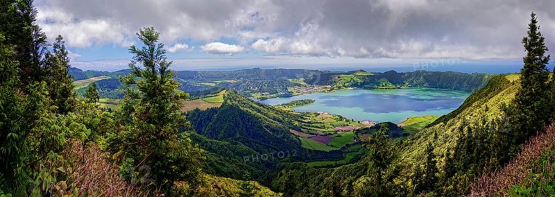 Wide panorama of the crater lake Lagoa Azul surrounded by lush green hills and clouds in the sky, crater circular hiking trail, Caldeira das Sete Cidades, Lagoa Azul, Sao Miguel, Portugal, Europe
