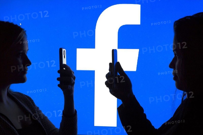 Silhouettes of two woman with smartphones in front of Facebook logo, 12.01.2016