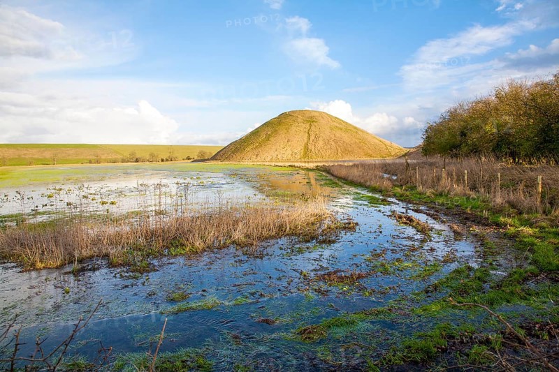 Silbury Hill ancient neolithic manmade chalk mound in Avebury, Wiltshire, England with flood water in the foreground