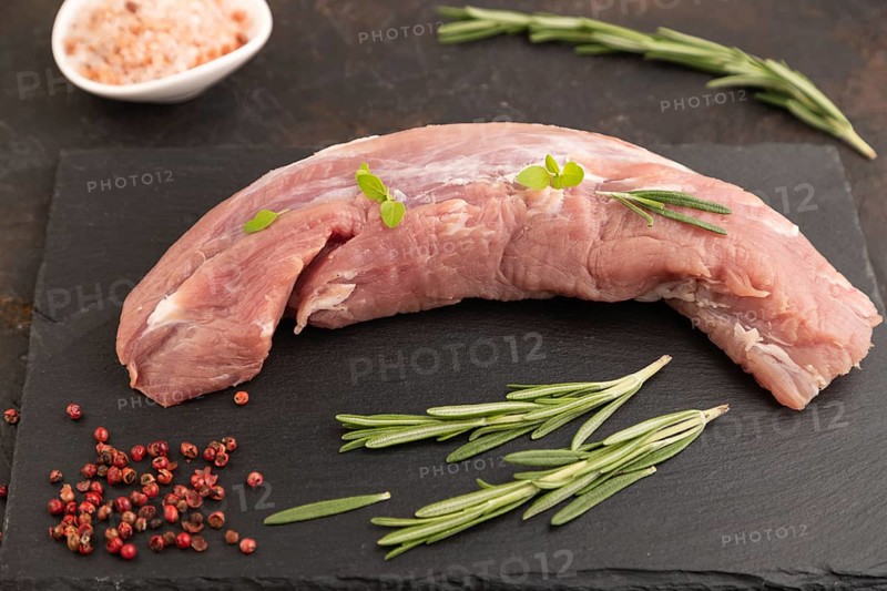 Raw pork meat with herbs and spices on slate cutting board on black concrete background. Side view, close up, selective focus