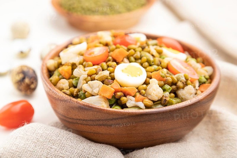 Mung bean porridge with quail eggs, tomatoes and microgreen sprouts on a white wooden background and linen textile. Side view, close up, selective focus