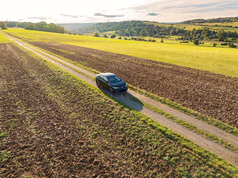 A black car drives along a country lane, surrounded by vast fields under a cloudy sky, Carsharing, VW ID5, Calw, Black Forest, Germany, Europe