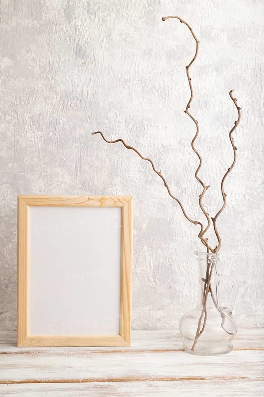 White wooden frame mockup with dried wine branch in glass on gray concrete background. Blank, vertical orientation, still life, copy space
