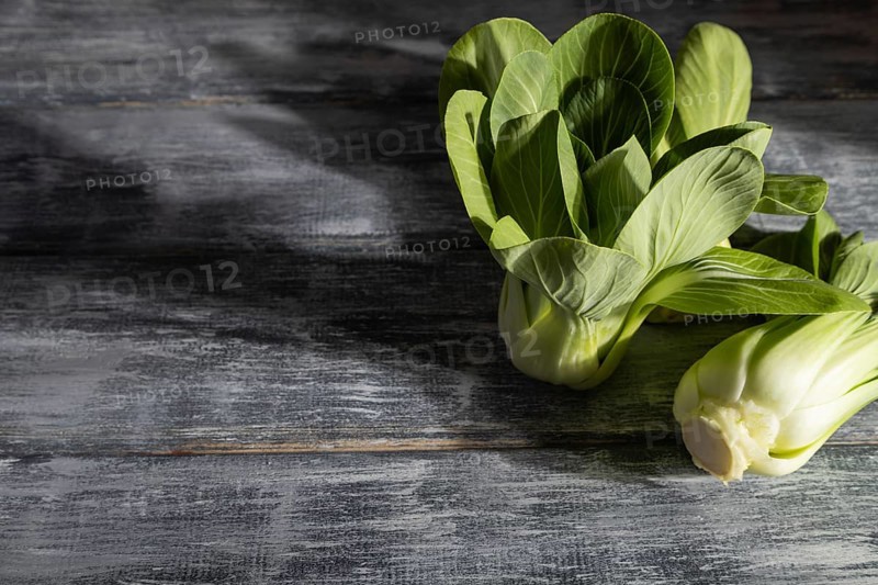 Fresh green bok choy or pac choi chinese cabbage on a gray wooden background. Hard light, contrast. Side view, copy space