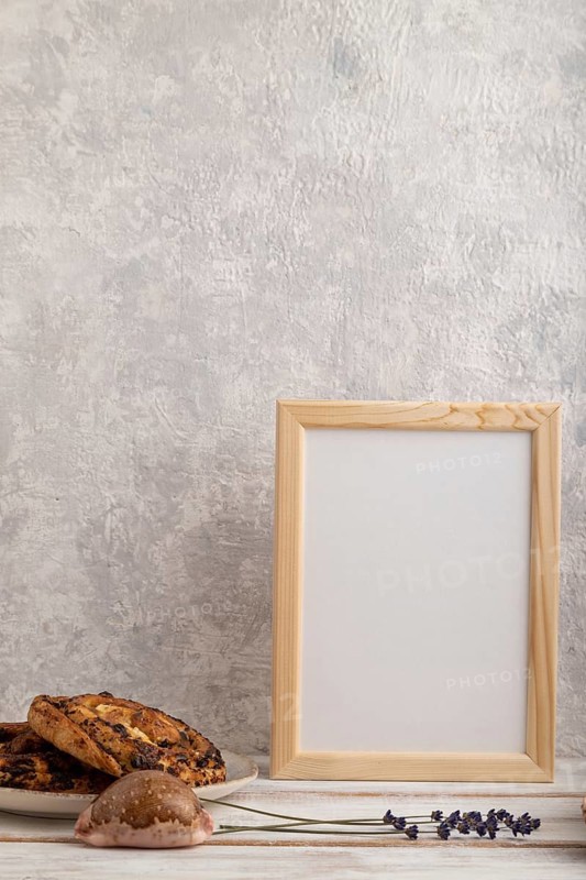 White wooden frame mockup with lavender in ceramic vase, linen textile, cup of coffee and bun on gray concrete background. Blank, vertical orientation, still life