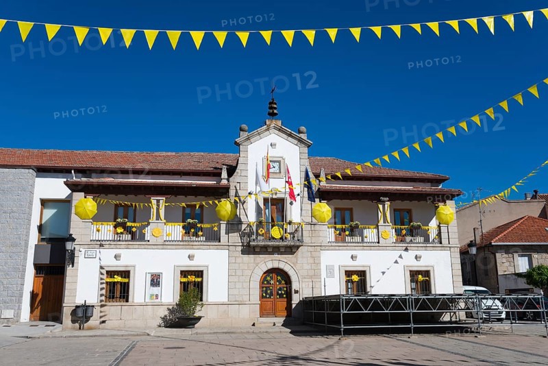 Historic building on a sunny square with yellow flags and festive decorations under a blue sky, City Hall, Los Molinos, Cuenca del Guadarrama, Madrid, Spain, Europe