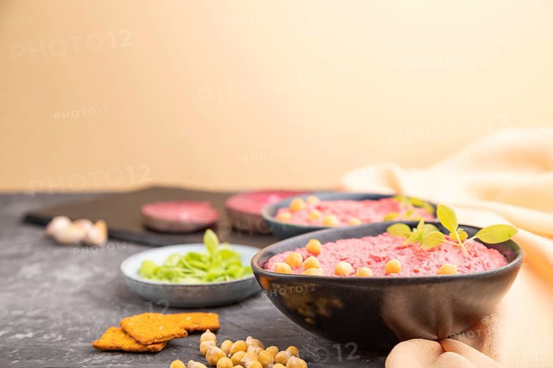Hummus with beet and microgreen basil sprouts in ceramic bowl on a black concrete background and orange textile. Side view, copy space, selective focus
