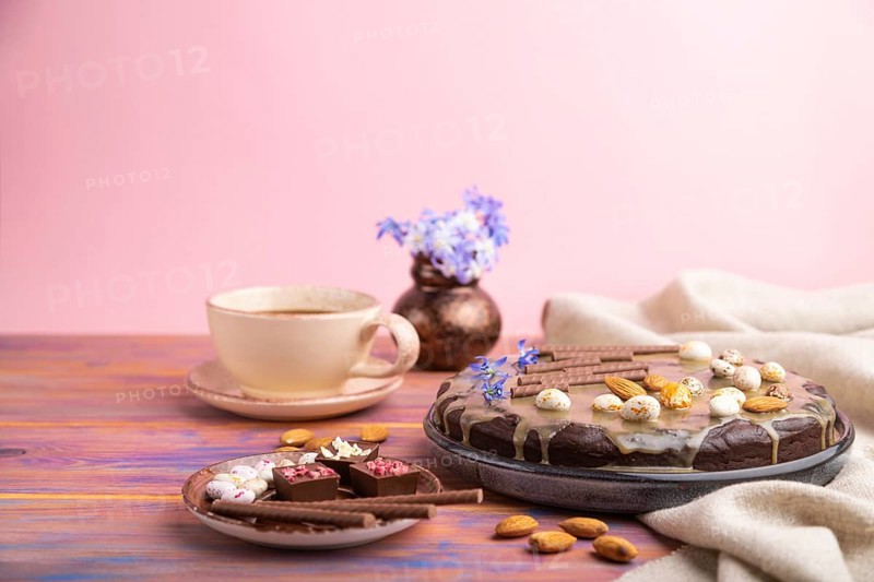 Homemade chocolate brownie cake with caramel cream and almonds with cup of coffee on a colored and pink background and linen textile. Side view, copy space, selective focus