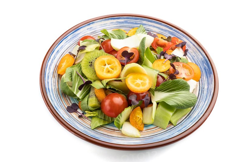 Vegetarian salad of pac choi cabbage, kiwi, tomatoes, kumquat, microgreen sprouts isolated on white background. Side view, close up