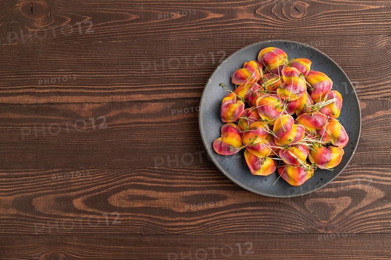 Rainbow colored dumplings with pepper, herbs, microgreen on brown wooden background. Top view, flat lay, copy space