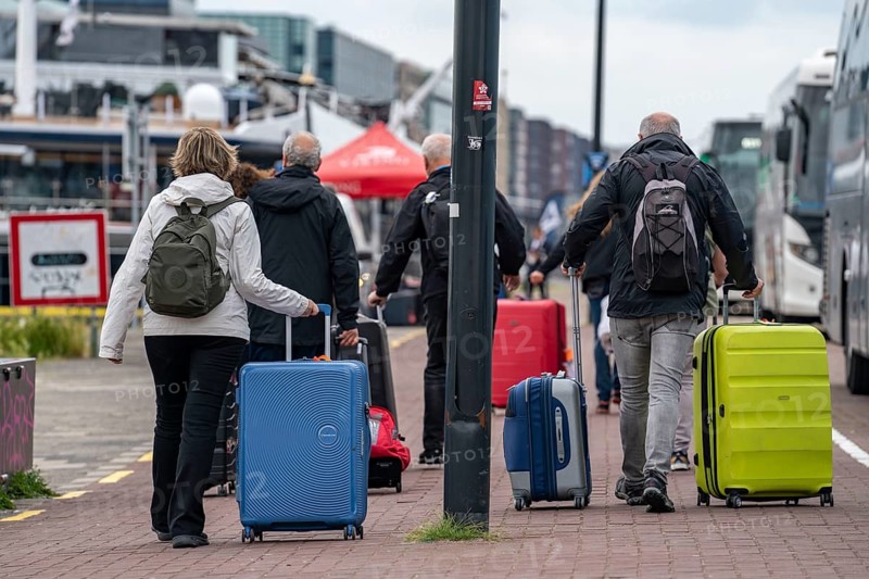 Travellers on their way to a river cruise ship at the quay of the Ij, transporting their luggage, wheeled suitcases, from the central station to the ship, Amsterdam, Netherlands