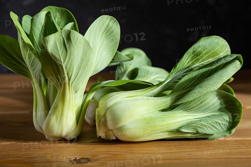 Fresh green bok choy or pac choi chinese cabbage on a gray wooden background. Hard light, contrast, dark, moody. Side view, close up, selective focus