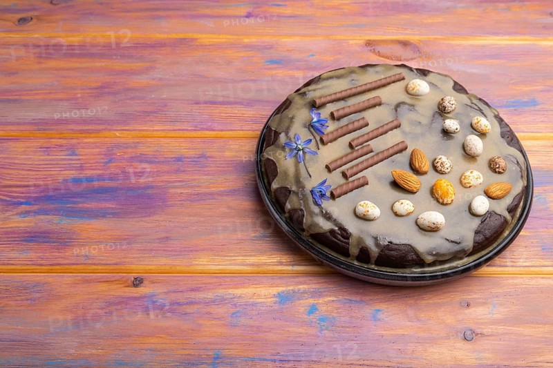 Homemade chocolate brownie cake with caramel cream and almonds on a colored wooden background. Side view, copy space, close up