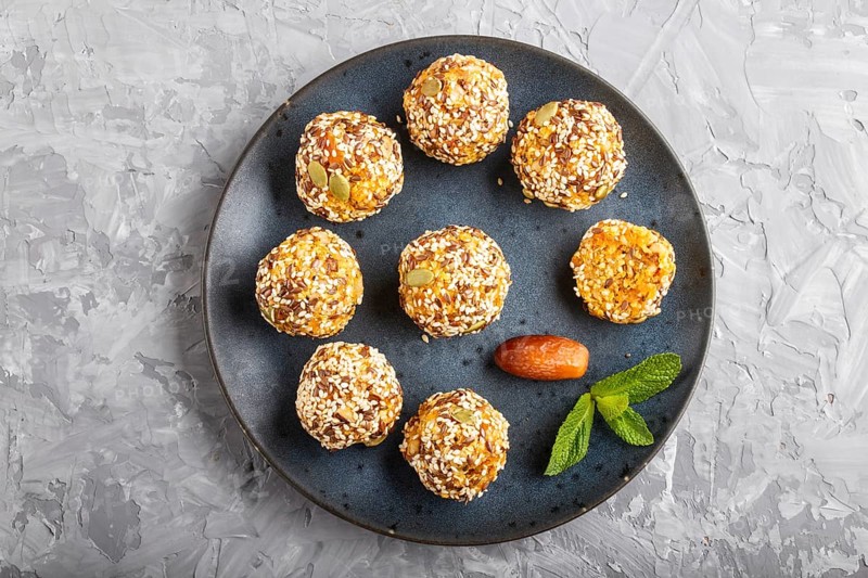 Energy ball cakes with dried apricots, sesame, linen, walnuts and dates with green mint leaves on a blue ceramic plate on a gray concrete background. top view, close up, flat lay. vegan homemade candy