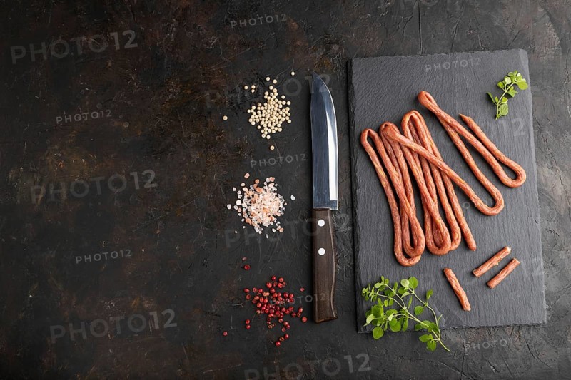 Traditional polish smoked pork sausage kabanos on a slate cutting board with salt and pepper on black concrete background. Top view, flat lay, copy space