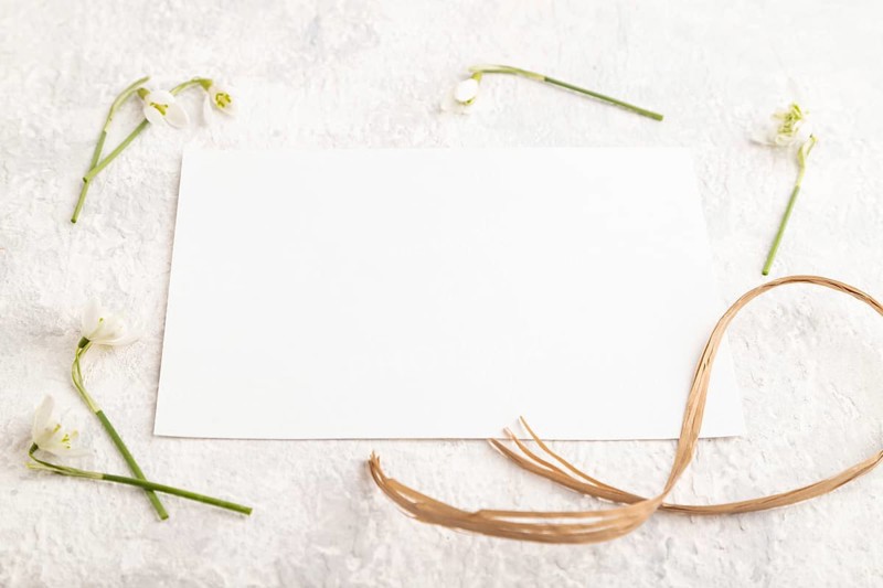 White paper sheet mockup with spring snowdrop galanthus flowers on gray concrete background. Blank, business card, side view, copy space, still life. spring concept