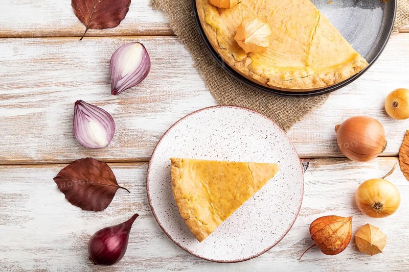 Autumn onion pie decorated with leaves and cup of coffee on white wooden background and linen textile. Top view, flat lay, close up