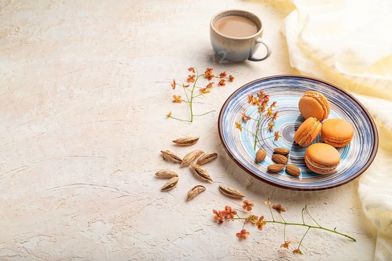 Orange macarons or macaroons cakes with cup of coffee on a white concrete background and linen textile. Side view, copy space