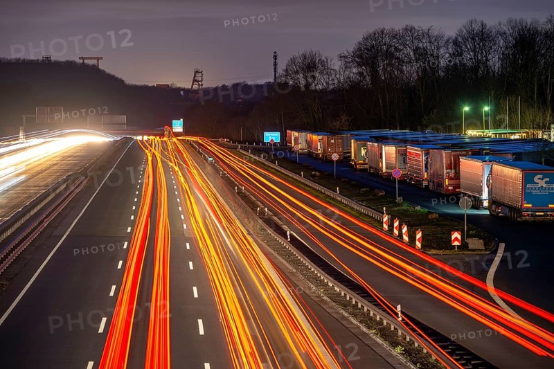 Evening traffic on the A2 motorway at the Recklinghausen junction heading west, in the background the headframes of the former Ewald colliery, Hohenhorst rest area, overflowing with lorries, North Rhine-Westphalia, Germany, Europe