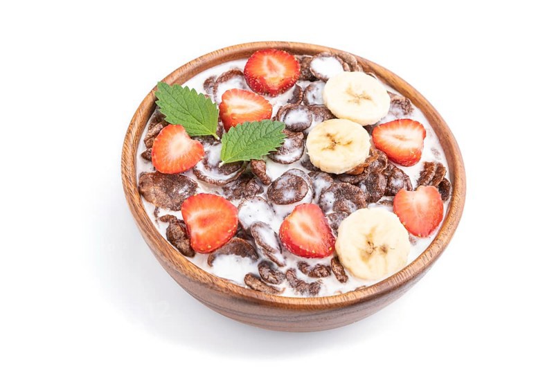 Chocolate cornflakes with milk and strawberry in wooden bowl isolated on white background. Side view, close up