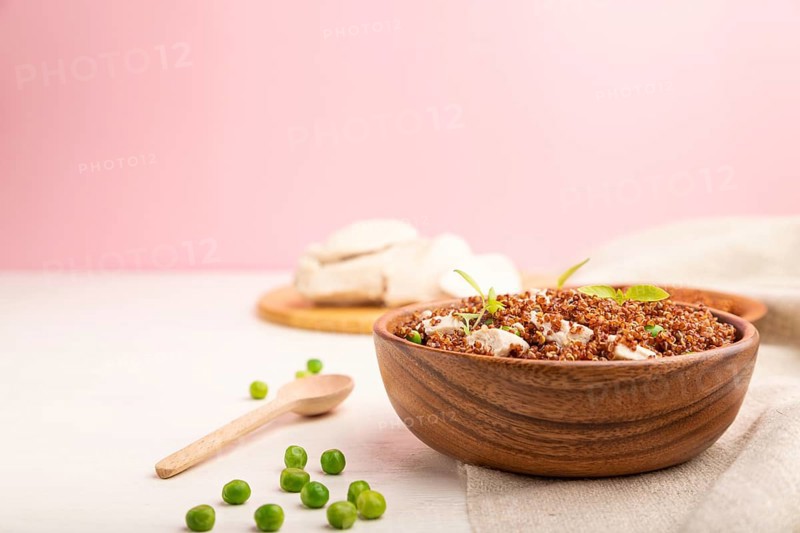 Quinoa porridge with green pea and chicken in wooden bowl on a white and pink background and linen textile. Side view, copy space, selective focus