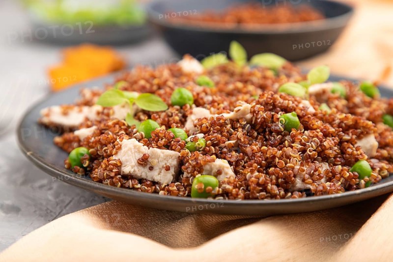 Quinoa porridge with green pea and chicken on ceramic plate on a gray concrete background and orange textile. Side view, close up, selective focus