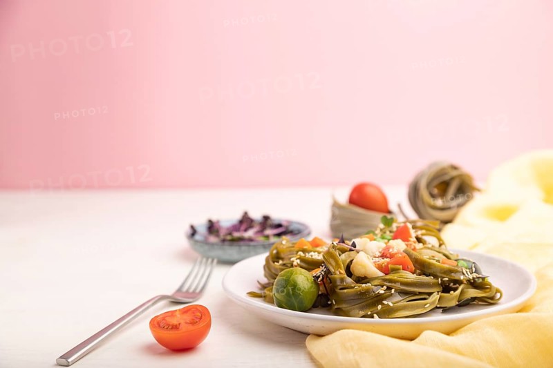 Tagliatelle green spinach pasta with tomato, pea and microgreen sprouts on a white and pink background and yellow textile. Side view, copy space, selective focus
