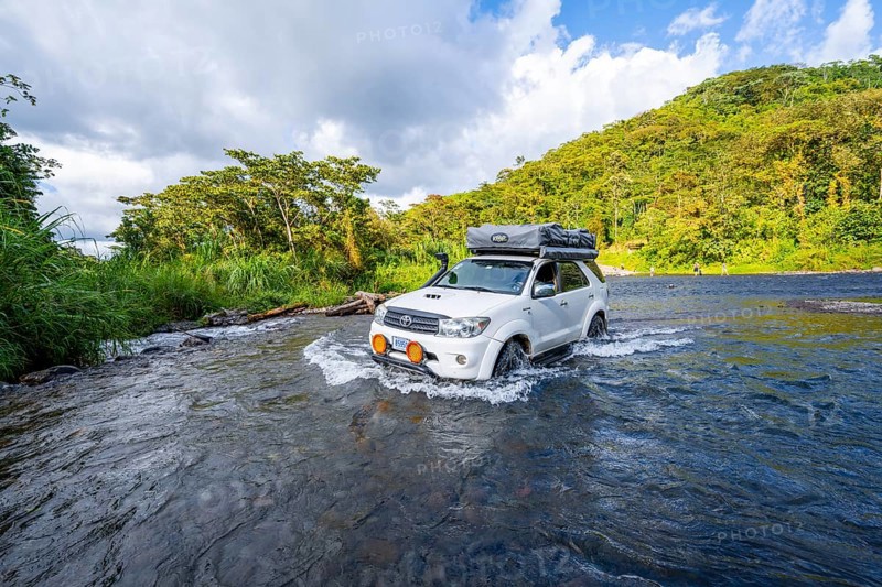 Toyota off-road vehicle with roof tent drives through a wide river in the rainforest, Alajuela province, Costa Rica, Central America