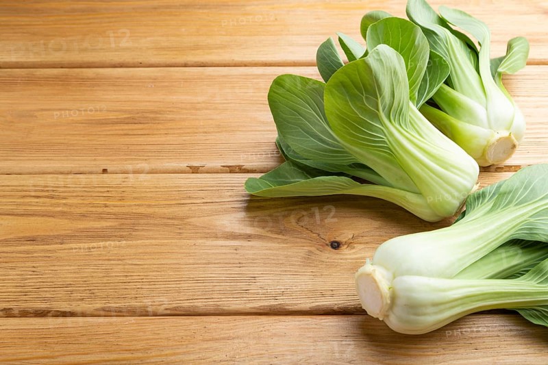 Fresh green bok choy or pac choi chinese cabbage on a brown wooden background. Side view, close up, copy space