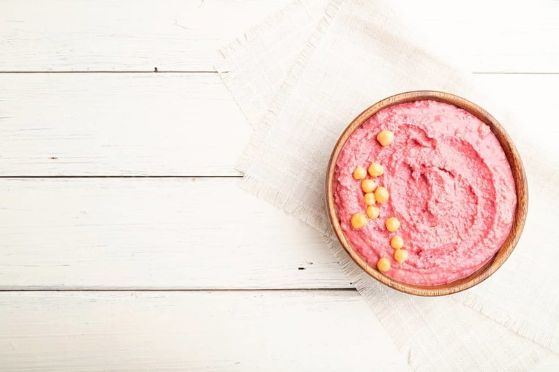 Hummus with beet in wooden bowl on a white wooden background and linen textile. Top view, flat lay, copy space