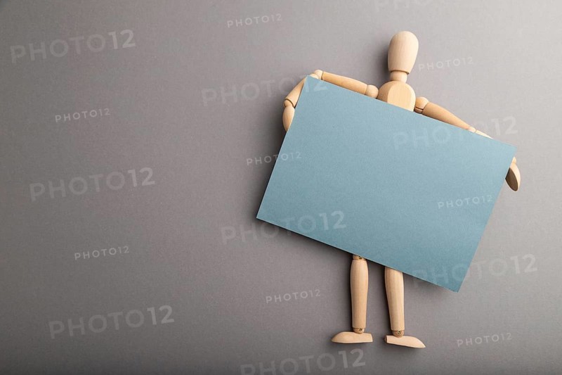 Wooden mannequin holding blue blank poster on gray pastel background. copy space, isolated, presentation concept