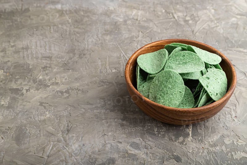 Green potato chips with herbs in wooden bowl on gray concrete background. Side view, copy space