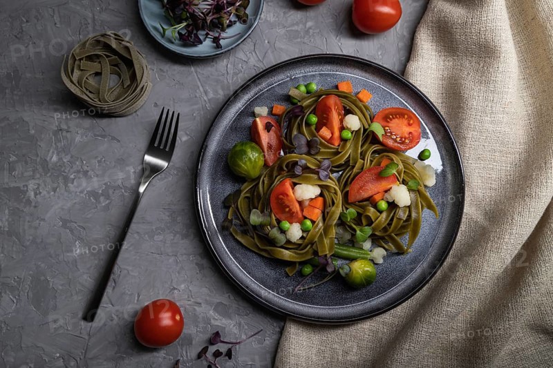 Tagliatelle green spinach pasta with tomato, pea and microgreen sprouts on a gray concrete background and linen textile. Top view, flat lay, close up, hard light