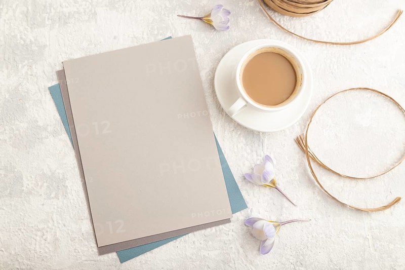 Gray paper sheet mockup with spring snowdrop crocus flowers and cup of coffee on gray concrete background. Blank, business card, top view, flat lay, copy space, still life. spring concept, close up