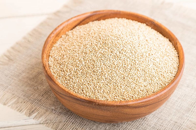 Wooden bowl with raw white quinoa seeds on a white wooden background and linen textile. Side view, close up, selective focus