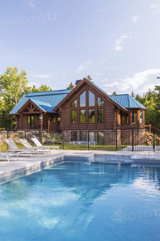 In-ground salt water swimming pool and brown stained milled Eastern white pine timber and flat log profile home facade with stone cladding on walk-out lower level and blue standing-seam sheet metal roof, Quebec, Canada, North America