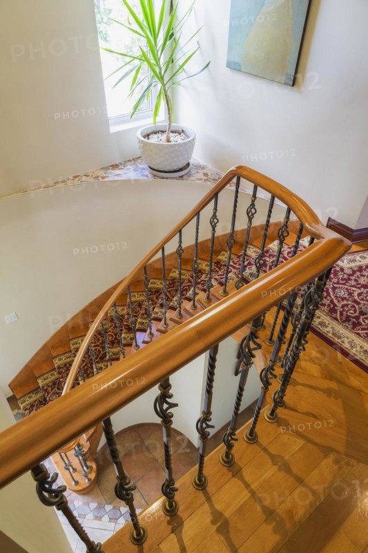 Top view of wooden spiraling staircase with burgundy and cream coloured rug runner and brass rods leading to upstairs inside a luxurious residential home, Quebec, Canada, North America