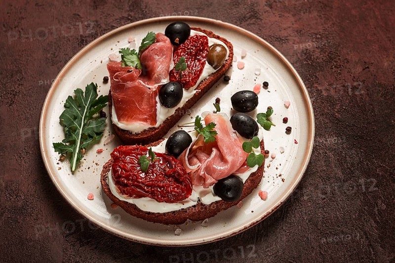 Sandwiches with cheese and prosciutto, dried tomatoes and olives, breakfast on a plate