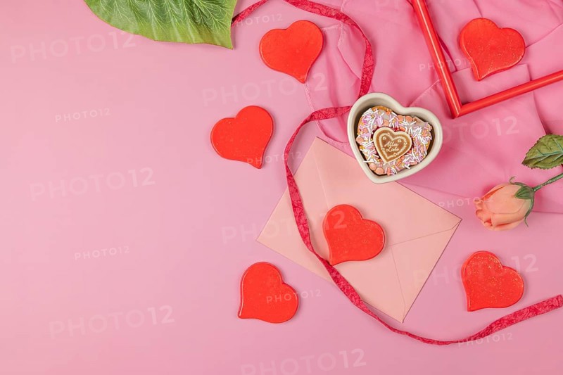 Bright red hearts scattered around a pink envelope and a single rose, Valentine's Day, heart-shaped cupcake, pink background