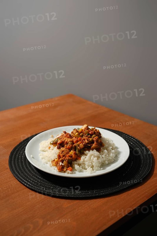 Homemade chicken stew with corn, peas, tomato, bell pepper and rice on wooden kitchen table
