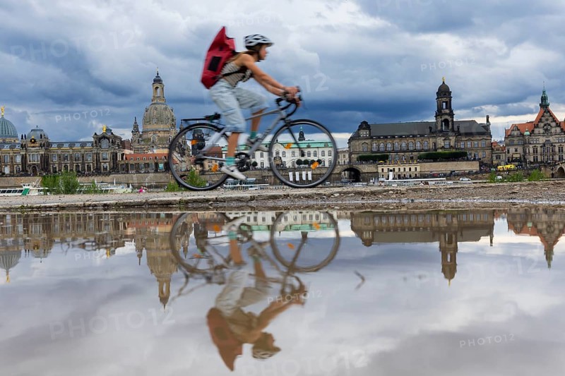 The Dresden silhouette with a cyclist and dark clouds behind the Church of Our Lady is reflected in a puddle on the Elbe cycle path, Elbe cycle path, Dresden, Saxony, Germany, Europe