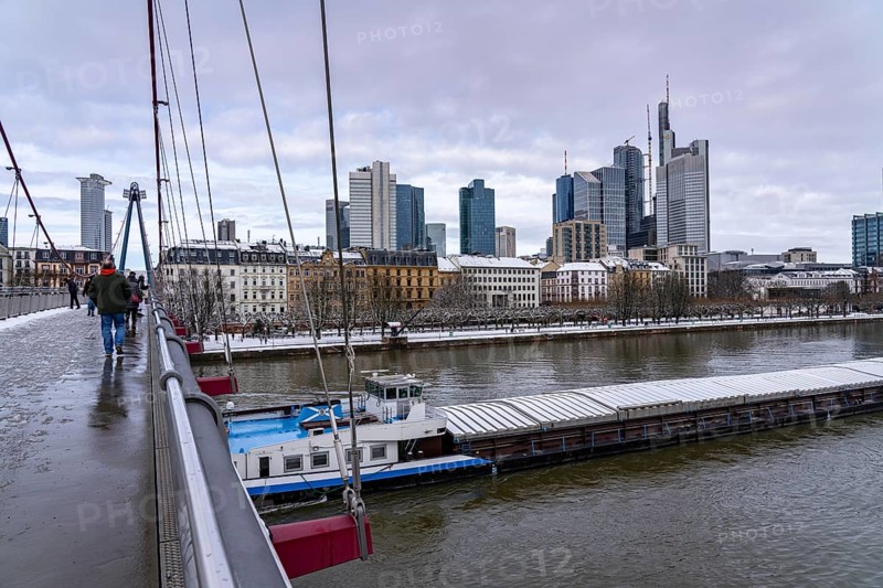 Winter in Frankfurt, view of the skyline of the city centre, from the Holbeinsteg foot and cycle bridge, freighter on the Main river covered in snow, Hesse, Germany, Europe