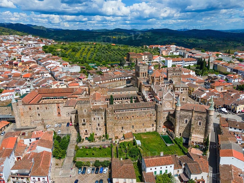 Aerial view of an old monastery with red roofs and surrounding green areas in a village in Spain. Historic architecture and scenic beauty. Aerial view, pilgrimage church and monastery, Real Monasterio de Nuestra Señora de Guadalupe, Guadalupe, Cáceres province, Caceres, Extremadura, Spain, Europe