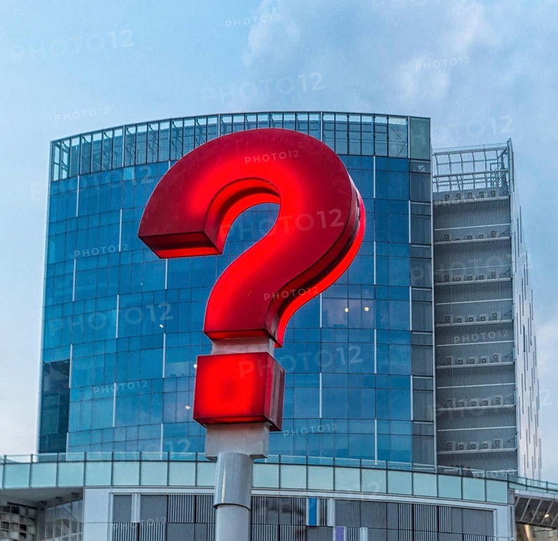 Red question mark on the streets of Singapore with a modern building in the background