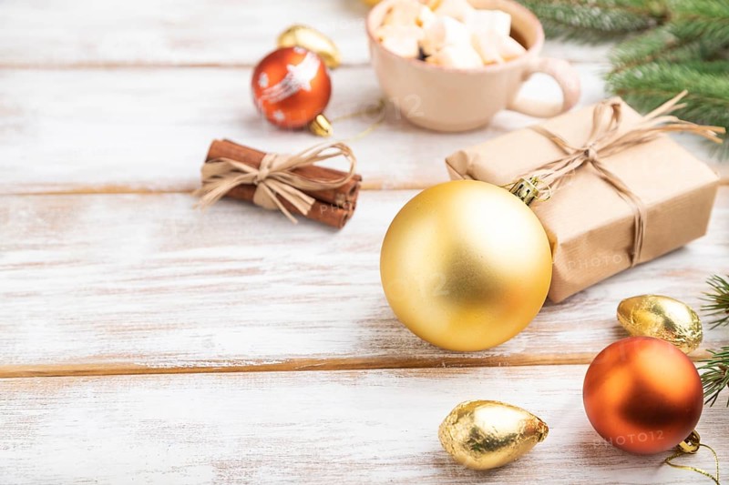 Christmas or New Year composition. Decorations, box, golden balls, cinnamon, fir and spruce branches, cup of coffee, on a white wooden background. Side view, copy space, selective focus